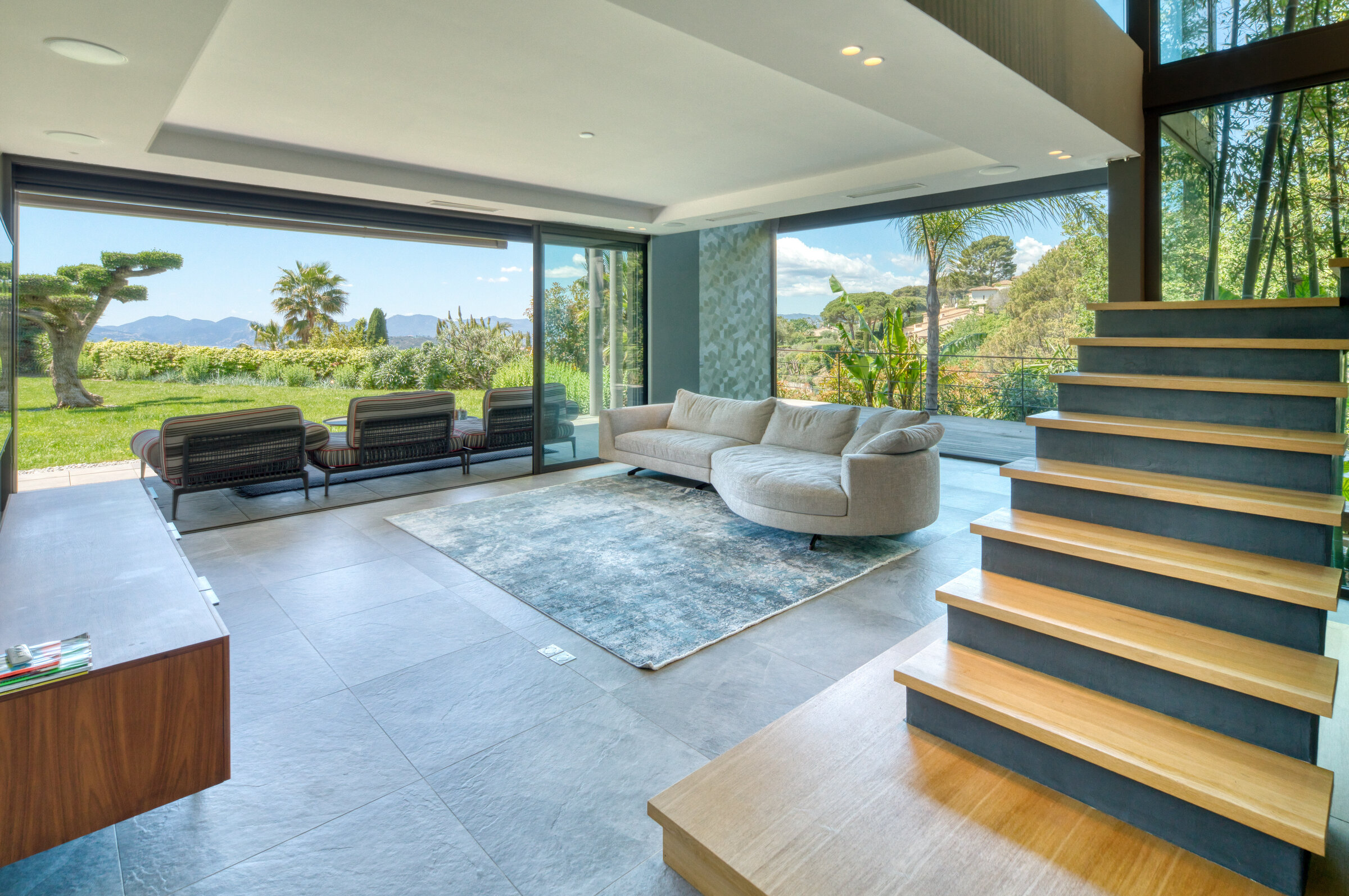 Salon ouvert avec canapé blanc, escalier et fenêtres pleine hauteur sur le jardin, Villa Bali